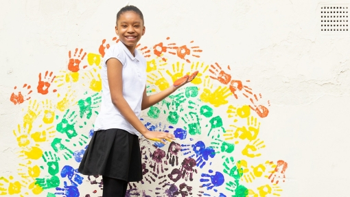 Girl standing in front of a white wall with handprints painted on the wall