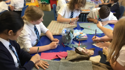 A group of young people sit around a table, colouring in with pencils and pieces of paper.