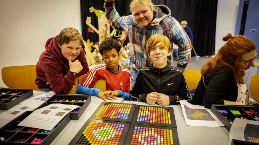 Young people looking happy in front of a table of beaded art work