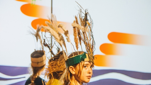 Young people perform on stage and they are wearing feathered headdresses.