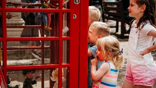 A photo of children looking into a red telephone box where puppets are on display.