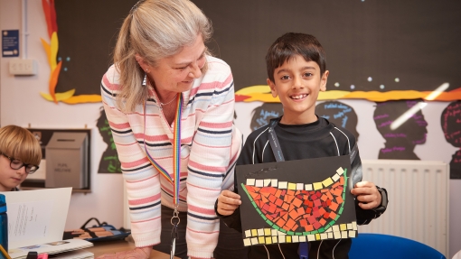 A pupil is holding up their art work and a teacher is next to him smiling. 