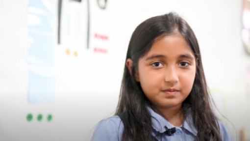 A person with long dark hair stands in front of a white wall decorated with colorful drawings and various decorations.