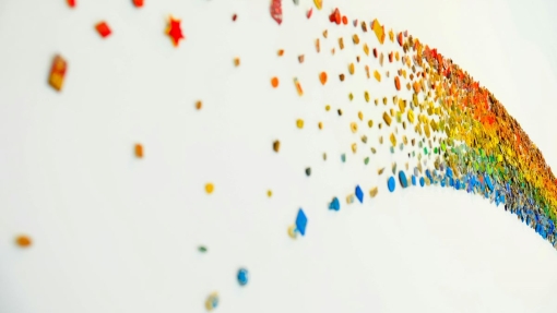 A curved rainbow pattern made of small, colorful objects on a white background. The objects include stars, circles, and irregular shapes, transitioning in color from red to purple.