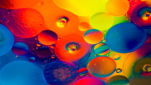 Abstract image with overlapping circles in bright colors—red, orange, yellow, green, blue, and purple—some translucent, some opaque, with small bubbles inside larger circles, creating a fluid, dynamic effect.