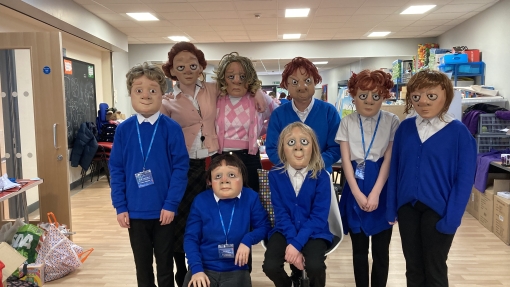 Seven children in blue sweaters and white shirts, wearing masks in a classroom 