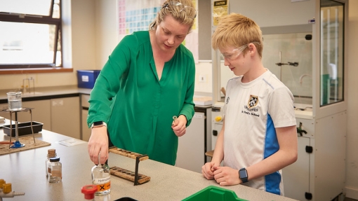A teacher in a green top is helping a student in a white t shirt do a science experiment