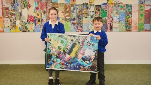 Two pupils holding up an abstract piece of art work. There is also a wall display behind them.