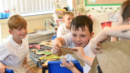 Child holding and examining a clay model in a classroom setting, with art supplies and colourful materials visible on the table. 