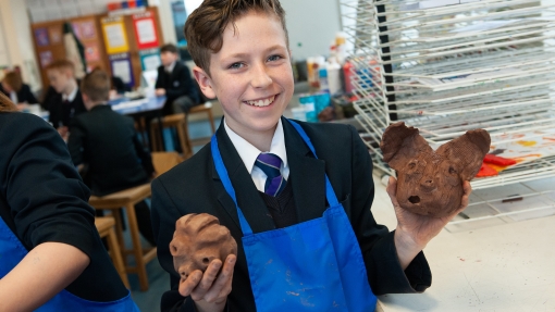 Male student proudly holds up pottery creatures