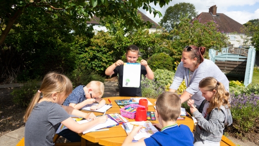 Group of students sitting outside at a table drawing with their teacher