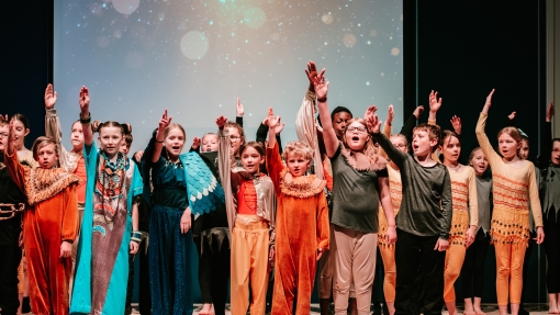 An image of a group of children stood on a stage in a variety of colourful costumes 