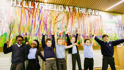 Young pupils standing in front of a colourful wall mural with their hands in the air 
