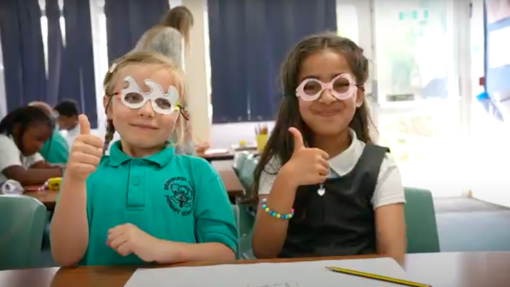 Two children sit down with their thumbs up
