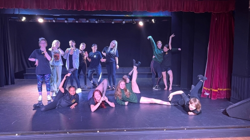 A group of young people pose in dance positions on a small stage.