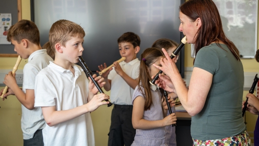 A teacher is showing a pupil how to play the recorder.
