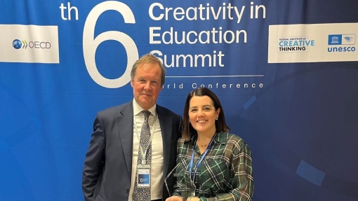 Two individuals with conference badges stand in front of a blue backdrop at the 6th Creativity in Education Summit, featuring OECD and UNESCO logos. One holds an award.
