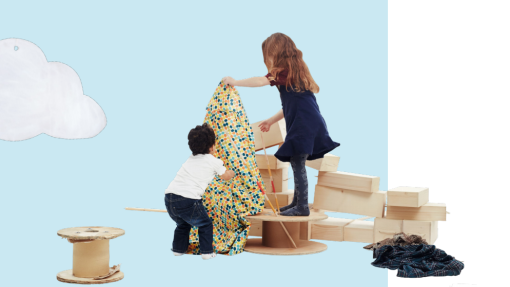 Two children play with a colorful patterned fabric, draping it over a large wooden spool. The child on the left wears a white shirt and jeans; the child on the right wears a navy blue dress and grey leggings. They are surrounded by wooden objects like spools and rectangular blocks, with a pile of plaid fabric on the floor to their right. The background is light blue with a cloud illustration in the top left corner.