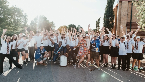 A group of adults and children are standing with their hands in the air outside