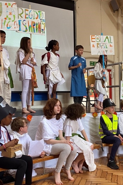 Year 4 performance about the life of Ghandi. A group of children stand on a stage in different coloured robes. 