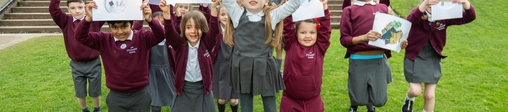 Students on the grass holding up art work, standing in front of a red brick building 