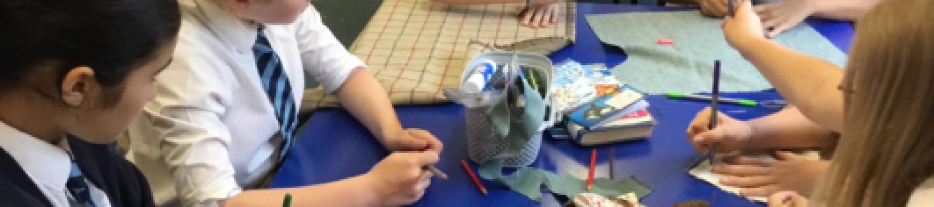A group of young people sit around a table, colouring in with pencils and pieces of paper.