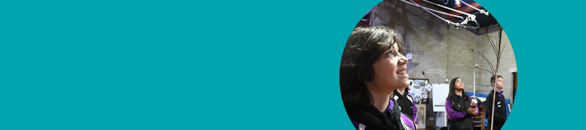 Photo from a circus workshop with a pupil in the foreground looking upwards. There are pupils in the background balancing plates on sticks
