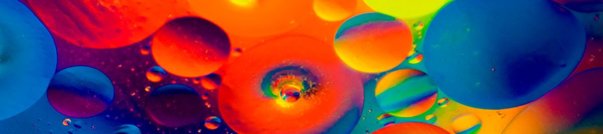 Abstract image with overlapping circles in bright colors—red, orange, yellow, green, blue, and purple—some translucent, some opaque, with small bubbles inside larger circles, creating a fluid, dynamic effect.