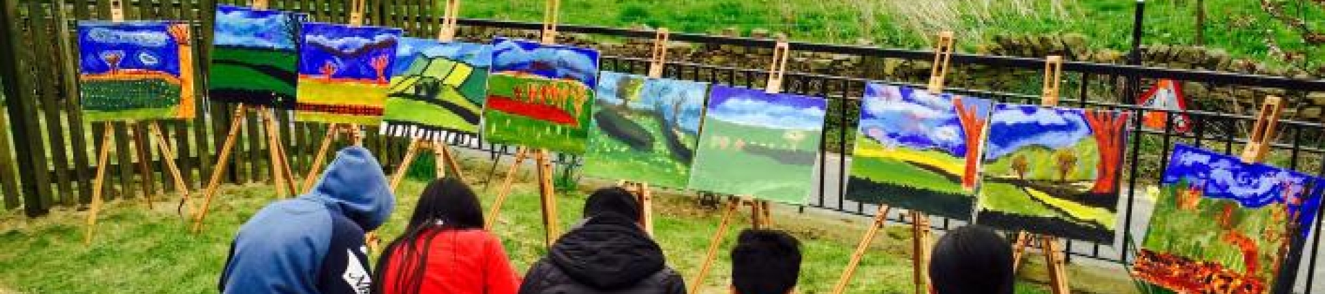 Children sitting on a bench facing a large field, drawing the landscape