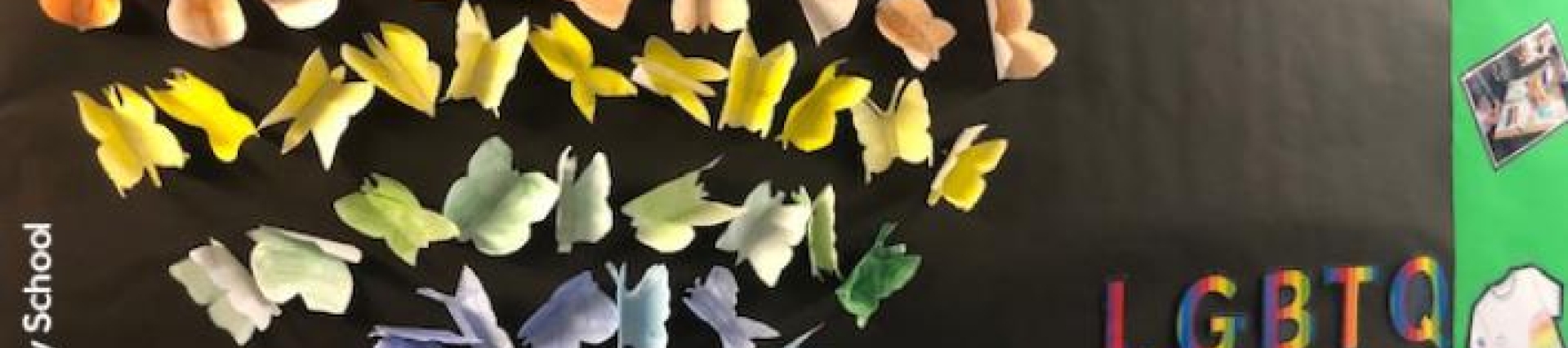 Paper origami diplayed as a heart on a black wall with LGBT written next to it