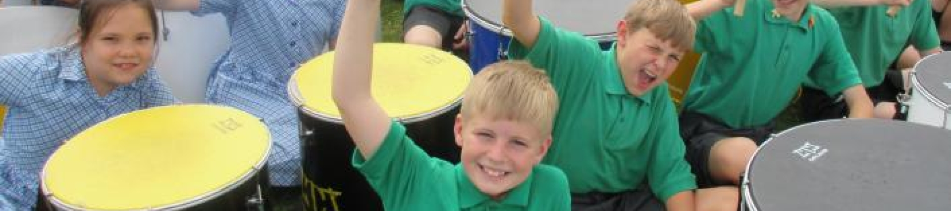 A group of pupils holding sitting with drums holding up their drum sticks