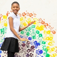 Girl standing in front of a white wall with handprints painted on the wall