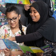 Two girls sitting in a library looking at a space themed booklet