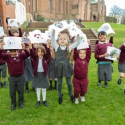 Students on the grass holding up art work, standing in front of a red brick building 