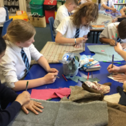 A group of young people sit around a table, colouring in with pencils and pieces of paper.