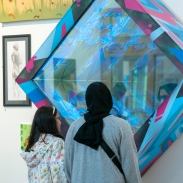 Two young girls stand with their backs to the camera, looking into a blue art instillation on a wall. 