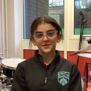 A young girl is sitting in a chair with a drum kit behind her