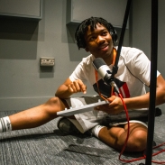 A young person sitting on the floor with a microphone in front of him and he's holding a piece of technical equipment.