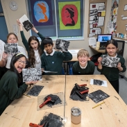A group of pupils at a desk holding up prints