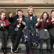 A group of students sitting Parliament with their teacher holding their thumbs up