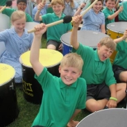 A group of pupils holding sitting with drums holding up their drum sticks 