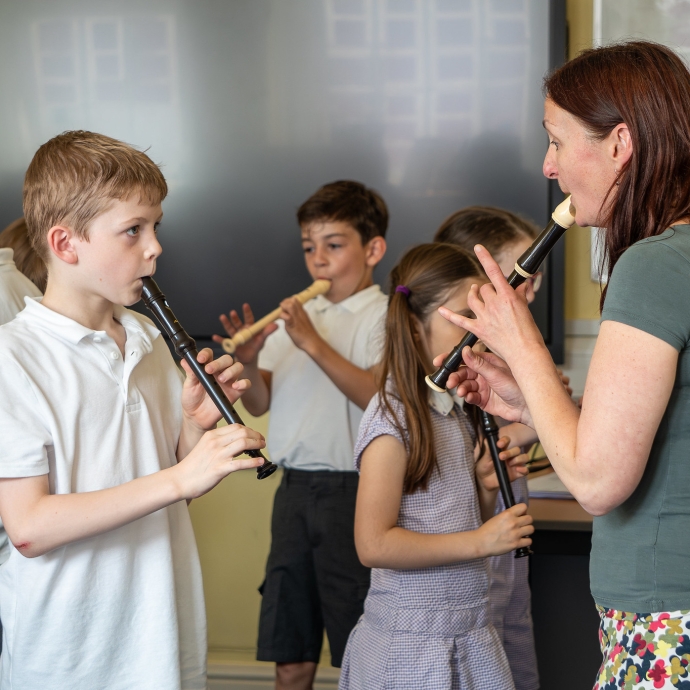 A teacher is showing a pupil how to play the recorder.